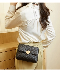 Detailed close-up of golden heart-shaped lock and quilted texture on a black chain bag