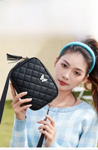Detail of a black quilted crossbody bag with white butterfly buckle and tassel fringe