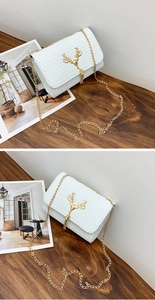 Detail of white textured crossbody bag featuring a gold deer head buckle and tassel chain