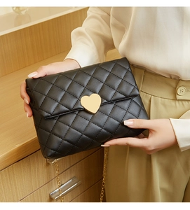 Close-up of black quilted shoulder bag featuring gold heart buckle and fine chain strap