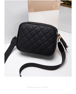 Close-up of black quilted camera bag with gold hardware, tassel and wide strap