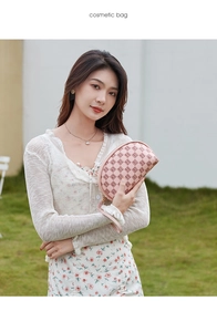 Detailed view of a pink letter pattern cosmetic bag with wristlet held by a model