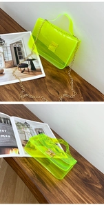 Detail of neon green transparent PVC bag with golden chain and metallic lock on wood