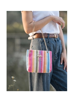 Close-up of rainbow woven straw bucket bag with gold chain and flamingo ornament