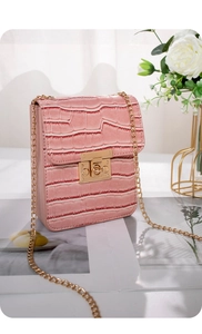 Close-up of pink faux crocodile leather bag with gold chain strap on art magazine