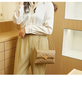 Detail of khaki quilted crossbody bag with golden heart-shaped lock and chain strap