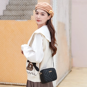 Quilted black crossbody camera bag with gold hardware shown on a stylish model outdoors