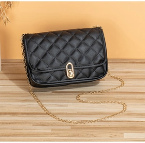 Detail of classic black quilted shoulder bag with golden twist lock on wooden surface
