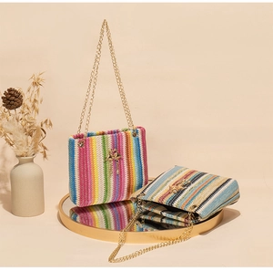 Detail of rainbow stripe woven straw bag with gold chain strap and bird charm decoration