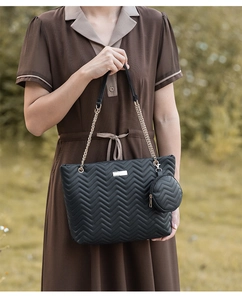 Detail of black quilted tote bag with V-shaped embroidery and gold chain strap accessory