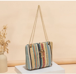 Detail of colorful striped woven tote bag with gold chain strap and bird pendant