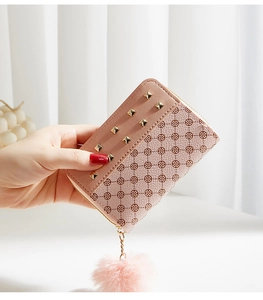 Detail of pink faux leather short wallet featuring gold studs and plush ball charm