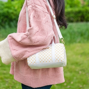 White Boston handbag with gold circle pattern and adjustable strap on a green grass backdrop