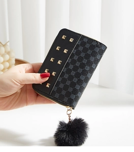 Detail of black leather wallet with gold studs, clover pattern, and faux fur pompom charm