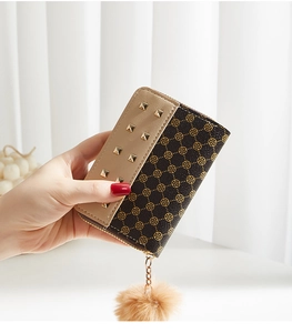 Detail of mini wallet with golden studs, geometric floral pattern and plush pom-pom charm