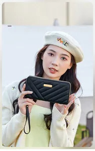 Detail of black quilted long zipper wallet with gold bar metal plaque and wristlet strap