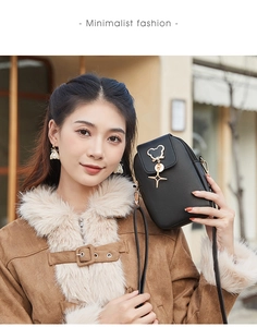 Detail of black leather crossbody phone bag featuring gold star and pearl charms