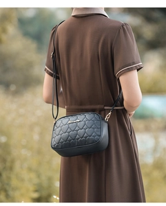 Detail of a black quilted heart crossbody bag with gold logo and adjustable strap