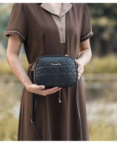Detail of black heart quilted crossbody bag featuring golden logo and adjustable strap