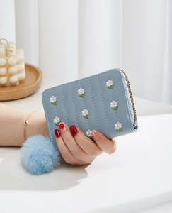 Close-up of light blue PU leather mini wallet with floral embroidery and plush ball