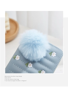Detail of light blue mini purse with floral embroidery and soft plush ball charm