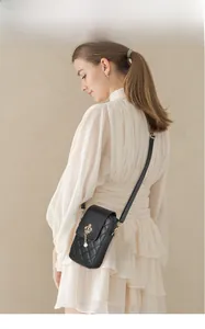 Crossbody phone bag with quilted black pattern, pearl crown detail, and thin shoulder strap