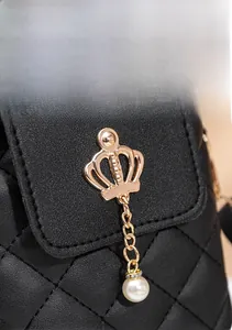 Detail of black quilted leather texture with gold crown charm and white pearl pendant