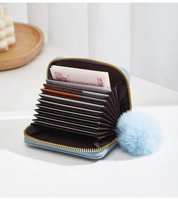 Détail d'un porte-cartes bleu en accordéon avec pompon en peluche et zip doré