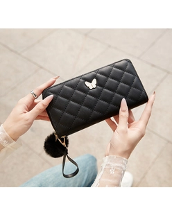 Close-up of black quilted long wallet with metal bow logo and soft plush pompom keychain