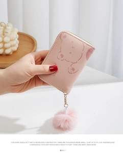 Porte-monnaie ours rose en peluche avec pompon doux tenu sur un fond esthétique apaisant