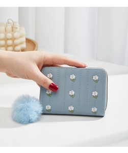 Close-up of light blue embroidered mini purse with a fluffy pompom keychain and zipper