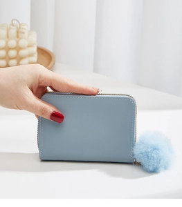 Detail of light blue mini wallet featuring floral embroidery and a matching pom-pom charm