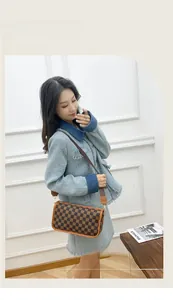 Brown checkerboard cylinder crossbody bag with wide shoulder strap worn by a model