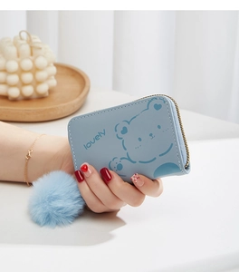 Gros plan du porte-monnaie bleu clair avec ours, zip doré et breloque pompon