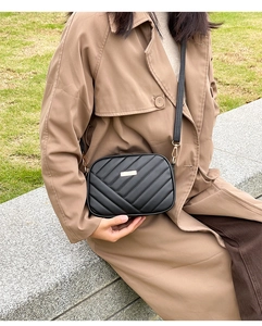 Quilted black crossbody camera bag with gold metal plate shown on a seated model in coat