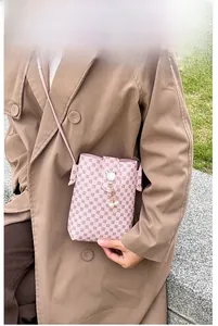 Pink crossbody phone bag with logo pattern and pearl tassel accessory in outdoor setting
