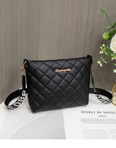 Detail of black quilted leather camera bag with gold hardware and stylish printed strap