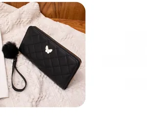 Close-up of quilted black leather wallet with golden butterfly and pompom on white knit
