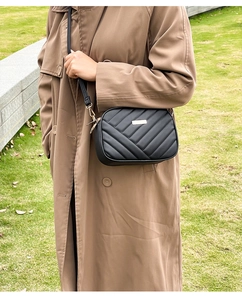 Close-up of black quilted camera bag with gold hardware worn over a brown trench coat