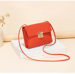 Close-up of orange quilted crossbody bag with golden metal lock on geometric stands