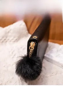 Detail of gold metal zipper and large black fluffy fur ball pompom on quilted leather wallet