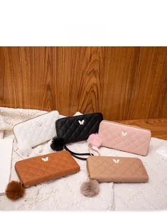 Close-up of quilted long wallets with butterfly metal decor and plush ball pendants