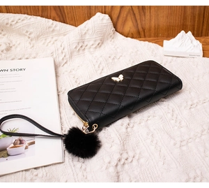 Close-up of quilted black long wallet with gold butterfly logo and plush pompom charm