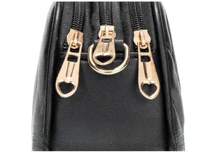 Detail of three golden zippers with heart-shaped pullers on a black leather shoulder bag