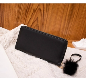 Detail of black long leather wallet featuring a fluffy pompom keychain and zip closure