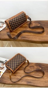 Detailed side view of a brown checkered cylinder bag with a wide fabric shoulder strap