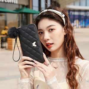 Quilted long wallet in black with bow charm and pompom pendant held by a model