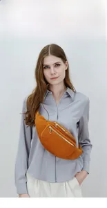 Close-up of orange corduroy fanny pack with dual gold zippers worn as a crossbody bag