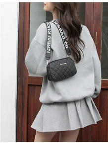Quilted crossbody camera bag with wide letter-print strap shown on shoulder