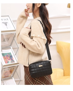 Close-up of black quilted camera bag with golden metal clasp and wide fabric strap
